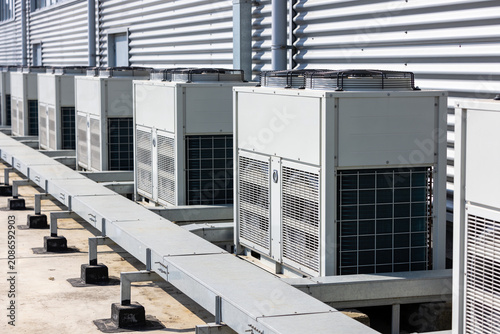 Row of industrial air conditioning units on a rooftop with corrugated metal siding