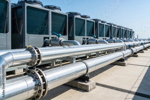 Industrial HVAC units and large pipes on a rooftop under a clear blue sky
