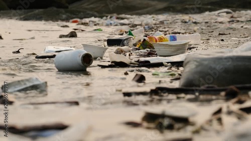 Plastic waste and plastic cups are washed up onto the beach by the sea. This highlights the concept of environmental problems and maintaining cleanliness.