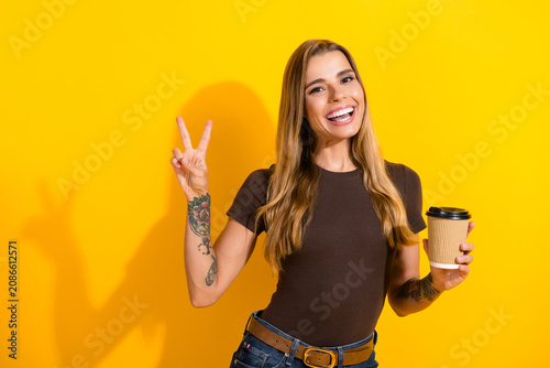 Canvas-taulu Smiling young woman holding a takeaway coffee cup and flashing a peace sign with
