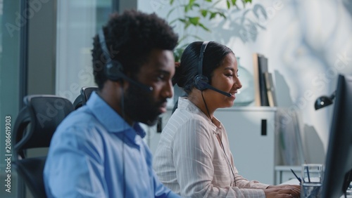 Two serious multiracial business colleagues working in call center consulting clients talking online consultation in agency. Team multiethnic coworkers man with woman callcenter operators talking chat