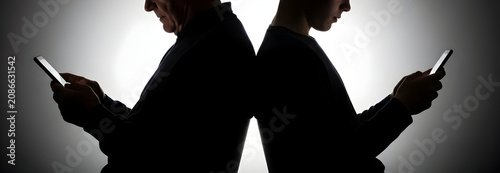 Silhouetted Man and Woman Interacting with Smartphones Against a Dark Background Indicating Modern Communication and Technology Isolation