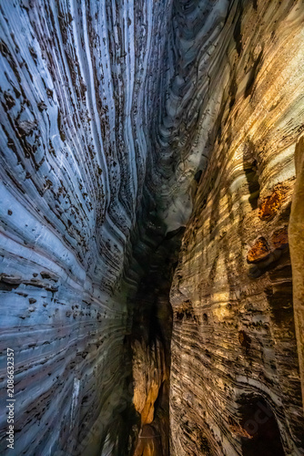 A narrow vertical chasm inside Blue Cave in Mae Sot, Tak, contrasts a brown rock wall with a stunning blue limestone layer, displaying an incredible natural geological wonder.
