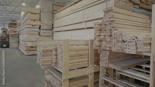Stacked wooden profiles with marked measurements stored on factory shelving for window frame production