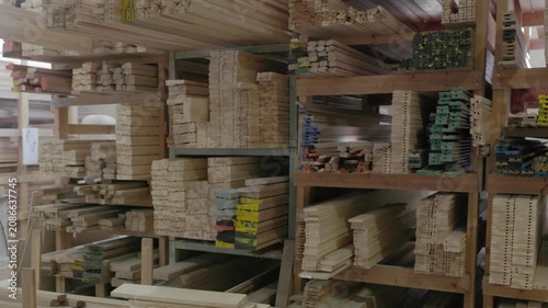 Stacked wooden profiles with marked measurements stored on factory shelving for window frame production