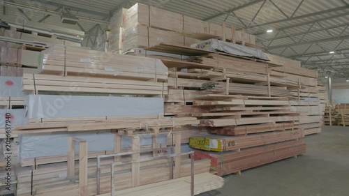 Stacked wooden profiles with marked measurements stored on factory shelving for window frame production