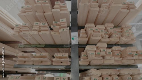 Stacked wooden profiles with marked measurements stored on factory shelving for window frame production