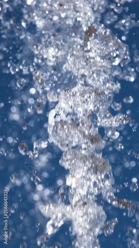 Close-up of sparkling fountain water splashes against clear blue sky. Refreshing droplets create dynamic abstract background representing freshness, summer, energy and motion