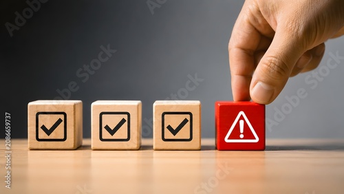 Hand selecting red block with warning alert triangle among checkmark blocks representing error detection and quality control anomaly