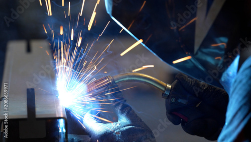Striking close-up of bright sparks flying from heavy industrial equipment during a metalworking process. The image captures the intense heat and dynamic energy of modern manufacturing
