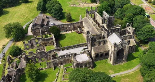 Aerial drone footage of Kirkstall Abbey in Leeds West Yorkshire England capturing the spectacular medieval Cistercian monastery ruins from above with surrounding parkland during the summer