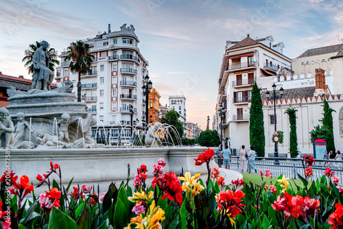 City fountain with flowers and people in Seville, Híspalis Fountain. People on streets city with beautiful architecture, an urban scene, Spain.