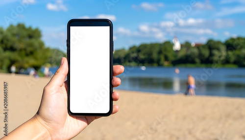 Hand Holding Smartphone With Empty Screen On Sunny Sandy Beach With Blurry People Background