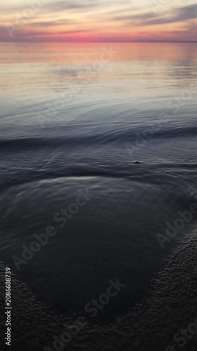 Sunset at the beach with gentle waves and calm water near the shore in a clear sky