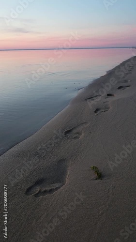 Footsteps on the sandy shore near the calm water at sunset in a natural coastal setting