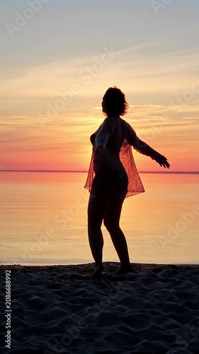 Vertical full shot of a woman silhouette dancing on the beach at vibrant sunset