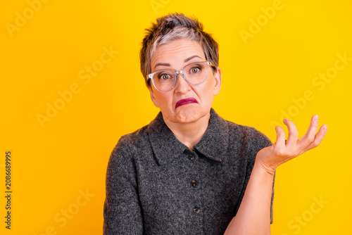 Fotografie Mature woman with glasses and gray hair making a confused shrug on bright yellow