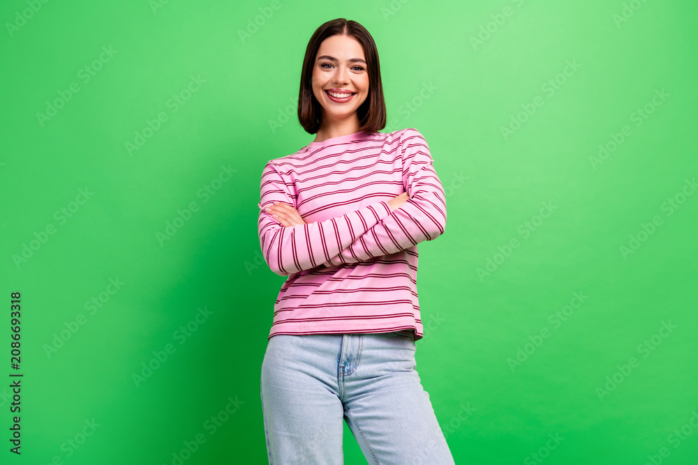 Naklejka premium Smiling young woman in striped pink shirt stands with confidence against a vibrant green background