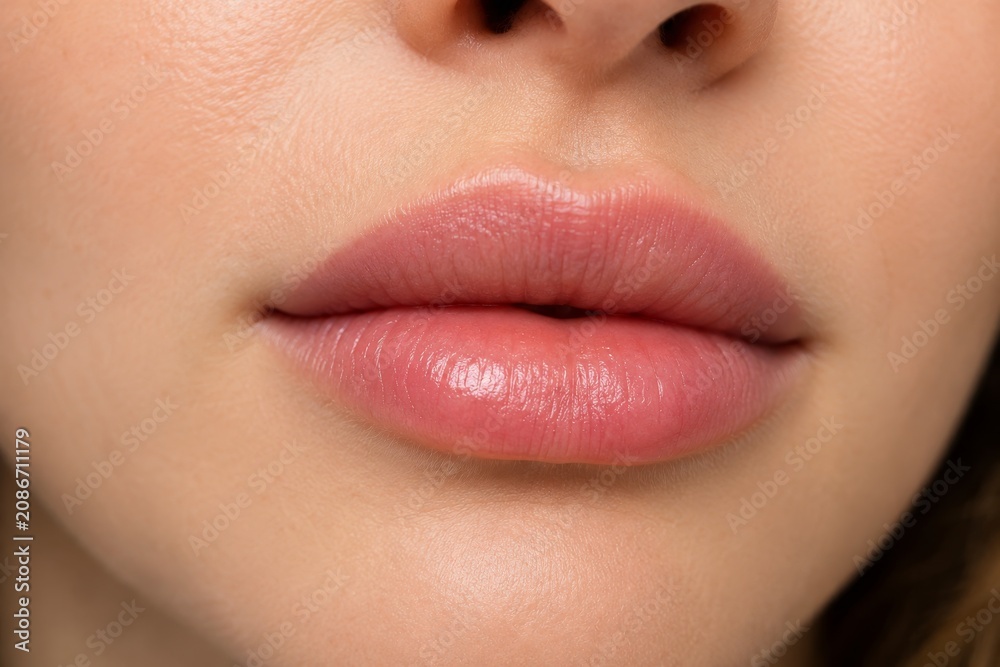 Obraz premium Woman lips after lip augmentation procedure. Close up of plump mouth with natural pink gloss. Aesthetic medicine treatment, dermal filler injection for lip contouring and rejuvenation.