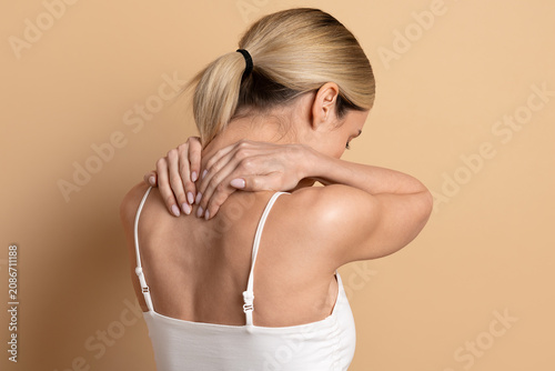 Fotografie Young beautiful woman massaging her neck and upper back on beige studio backgrou