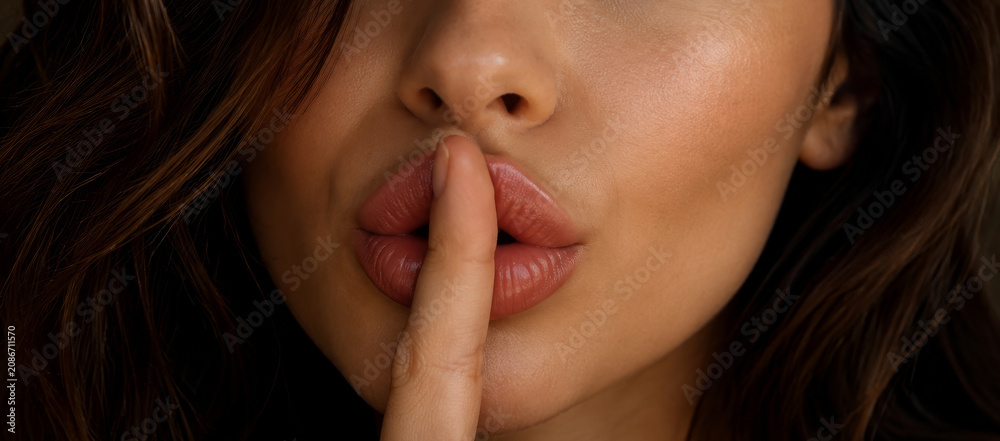 Fototapeta premium Woman with filler injection in lip showing hush gesture. Cosmetics procedure for beautiful lip shape. Professional beauty clinic service for facial rejuvenation and skin care concept.