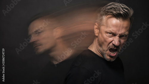 Middle-aged man shouting and showing anger with a motion-blurred double exposure effect on a dark background. The image conveys intense emotion and inner turmoil.