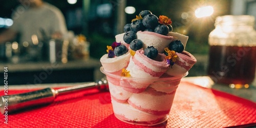 Thai rolled ice cream in a cup, topped with blueberries and edible flowers, street food aesthetic, vibrant colors.
