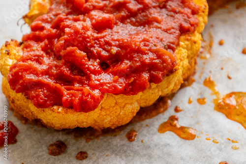 Close-up of golden roasted cauliflower steaks baked in a sheet pan, smothered with rich herb tomato sauce