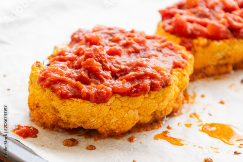 Close-up of golden roasted cauliflower steaks baked in a sheet pan, smothered with rich herb tomato sauce