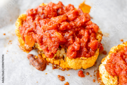 Close-up of golden roasted cauliflower steaks baked in a sheet pan, smothered with rich herb tomato sauce