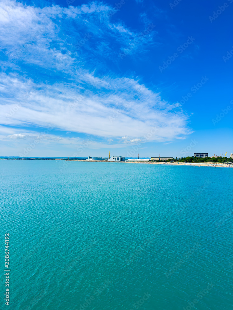 Fototapeta premium Clear blue water and sky over the harbor with boats and buildings in the distance during daytime