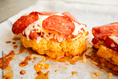 Close-up of a golden-baked cauliflower steak pizza, layered with rich tomato sauce, melted mozzarella cheese, and crispy salami slices on a baking sheet