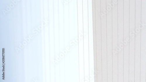 Abstract view of moving white window blinds in soft breeze.
