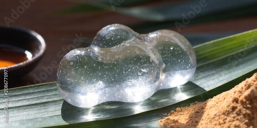 Japanese Raindrop cake (Mizu Shingen Mochi), clear as water, on a bamboo leaf, kinako powder and syrup on the side.