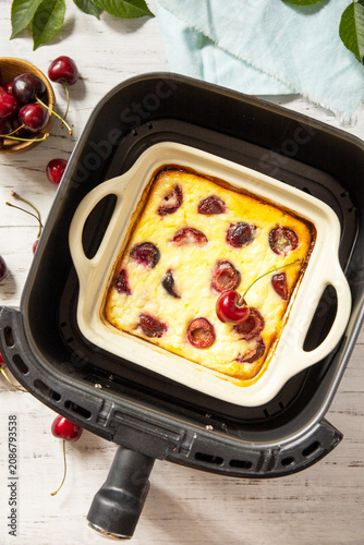 Homemade cottage cheese casserole with cherries in kitchen gadget modern air fryer on wooden background, perfect for breakfast or a snack. Top view flat lay background.