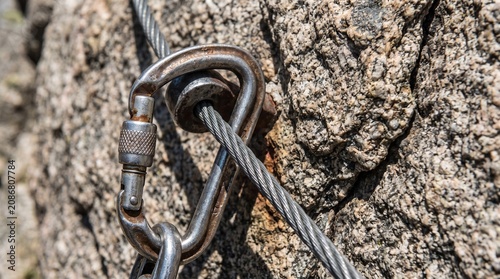 Climbing carabiner attached to a steel wire cable on a mountain rock face