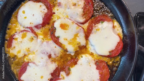 An appetizing close-up of delicious tomato slices, sizzling in a cast-iron skillet, topped with plenty of melted cheese and spices