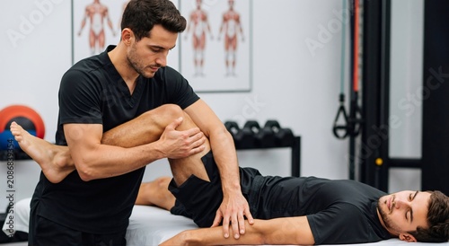Male physical therapist performing knee and leg stretch on man. Rehabilitation and chiropractic therapy for muscle and joint health. Manual treatment concept.