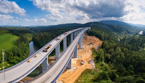 drone view major highway overpass construction site heavy machinery concrete pillars building new road bridge infrastructure expansion project beautiful green forest river landscape