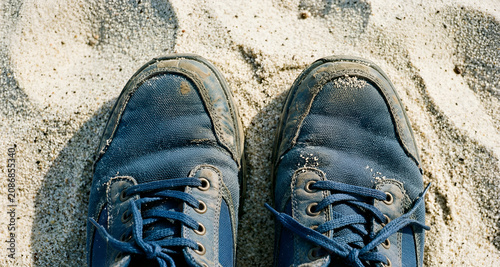 Vista da sopra in primo piano di vecchio e consunto  paio di scarpe sportive su una superficie di fine sabbia