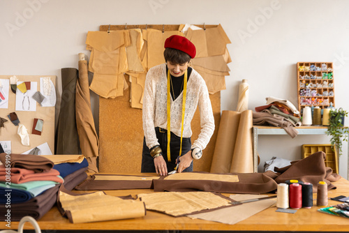 Foto Smiling female tailor cutting pattern on large worktable
