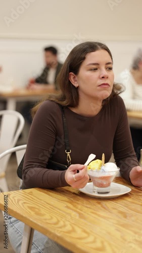 Young woman is sitting at a table in a cafe, eating delicious ice cream and drinking freshly squeezed juice. High quality 4k footage