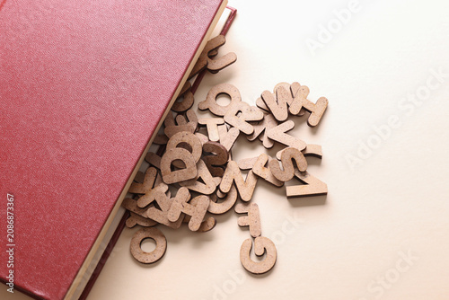 Book with many wooden letters on a beige background. Education, learning concept.