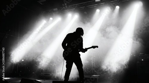Silhouette of a guitarist playing on a brightly lit stage with smoke effects.