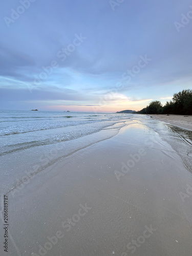 Vertical landscape of a quiet beach with gentle ocean waves and a moody cloudy sky reflecting on the shoreline.