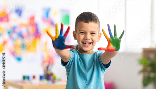 Happy little child showing colorful painted hand at camera, messy fingers covered in vibrant paint, enjoying creative art activity for early childhood