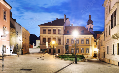 Hungary - Cozy little baroque square in the center of Gyor, with the bronze sculpture of Nimrod, in the background the Cathedral tower at night