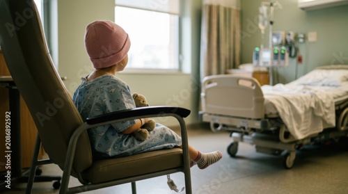 Young child in hospital gown and pink beanie sitting in a chair