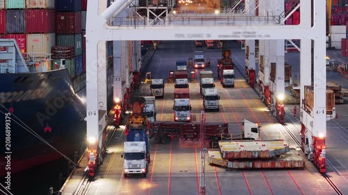 gantry crane loading cargo container from truck to container ship at busy industrial harbor port terminal. Global maritime logistics, freight transportation, and international supply chain trade.