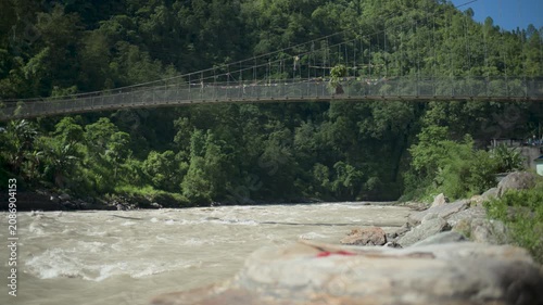 Traditional Footbridge Suspension Bridge Over Fast Flowing Muddy River in Mountains